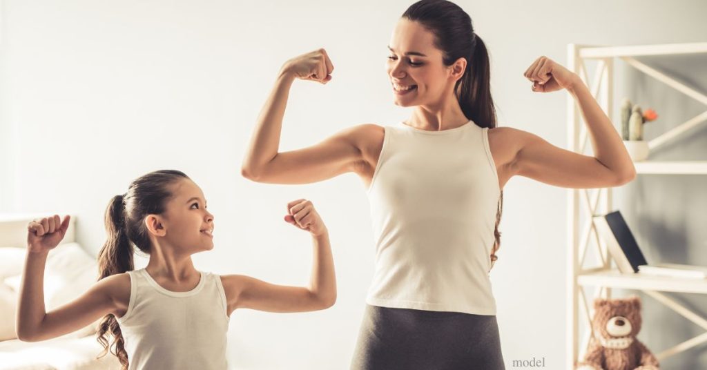 A mom and her daughter are wearing light colored tank tops and flexing their muscles. (models)
